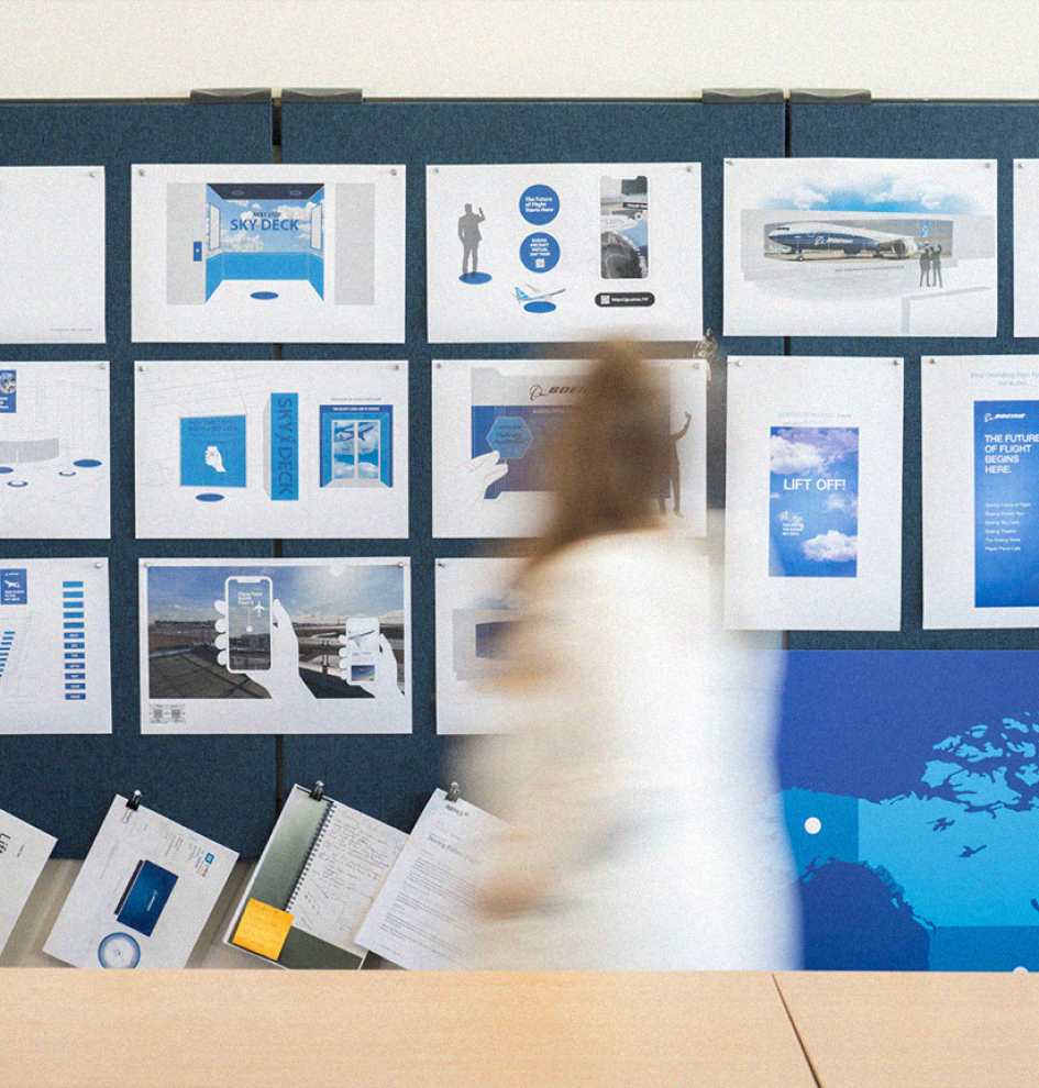 A DCG ONE employee walks in a blur past a wall covered in printouts of signage and augmented reality mock-ups.